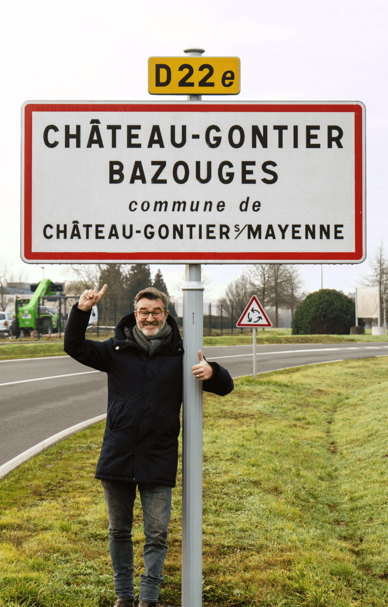 Stan de Vion fondateur de Stan Bio posant fièrement devant le panneau de Château-Gontier sur Mayenne lieu de fabrication des croquettes bio