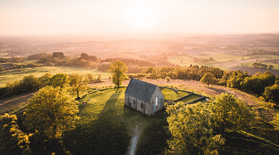 Chapelle en Mayenne isolée sur une colline verdoyante au coucher du soleil illustrant le territoire de production des croquettes bio Stan Bio