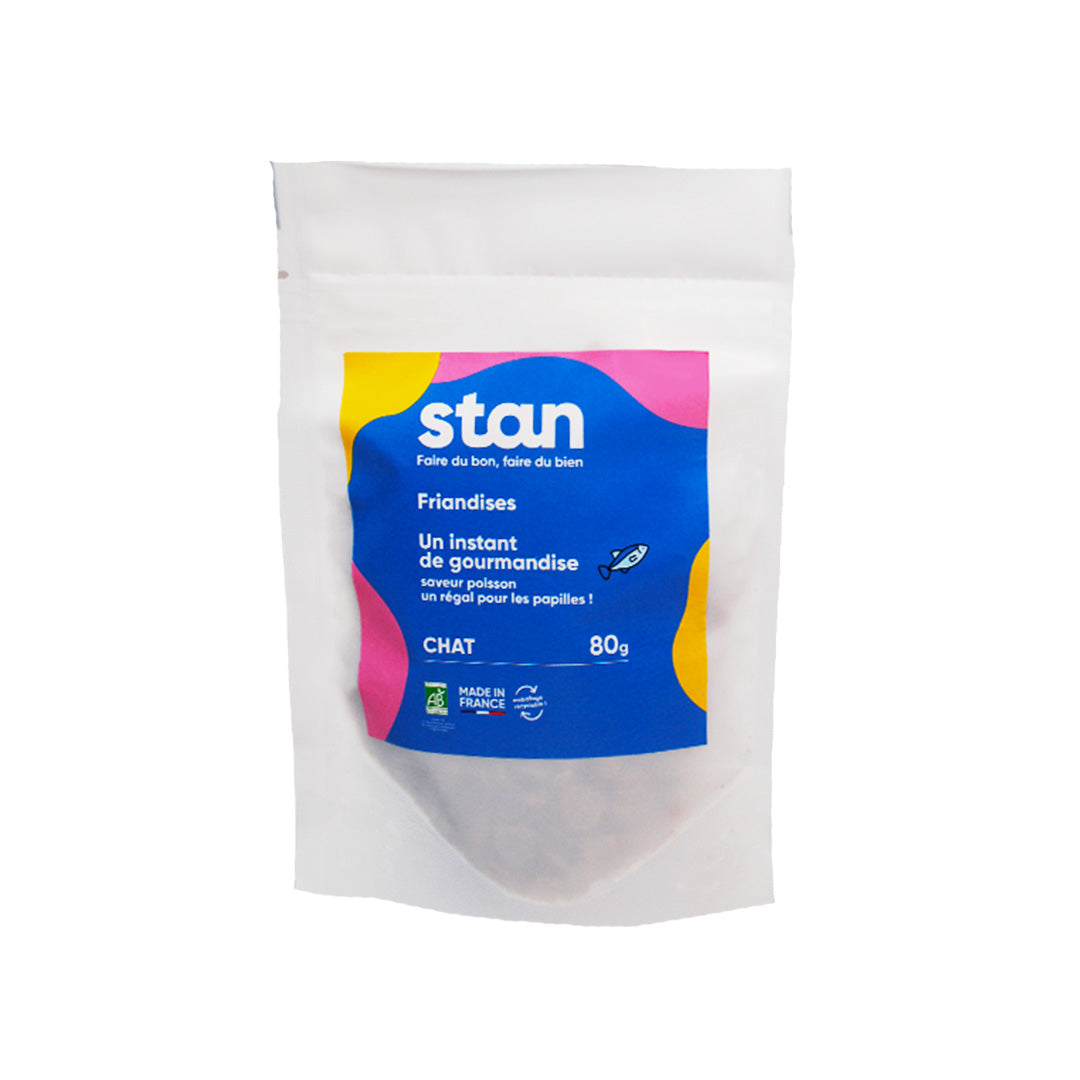 Un sachet de friandises naturelles pour chat est au centre de l’image. Le sachet contient des friandises bio au bon goût de poisson et fait 80 grammes.