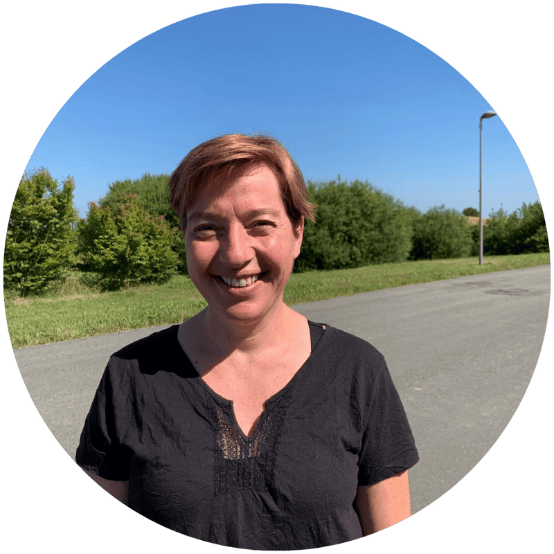 Magali, chargée de l'administration et de la qualité chez Stan.bio, souriante en t-shirt noir, photographiée en extérieur avec un fond de végétation