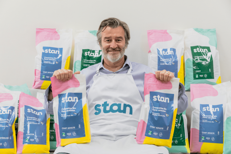 Stan de Vion fondateur de Stan Bio portant son tablier de marque et tenant fièrement ses sachets de croquettes bio chiens et chats devant toute la gamme