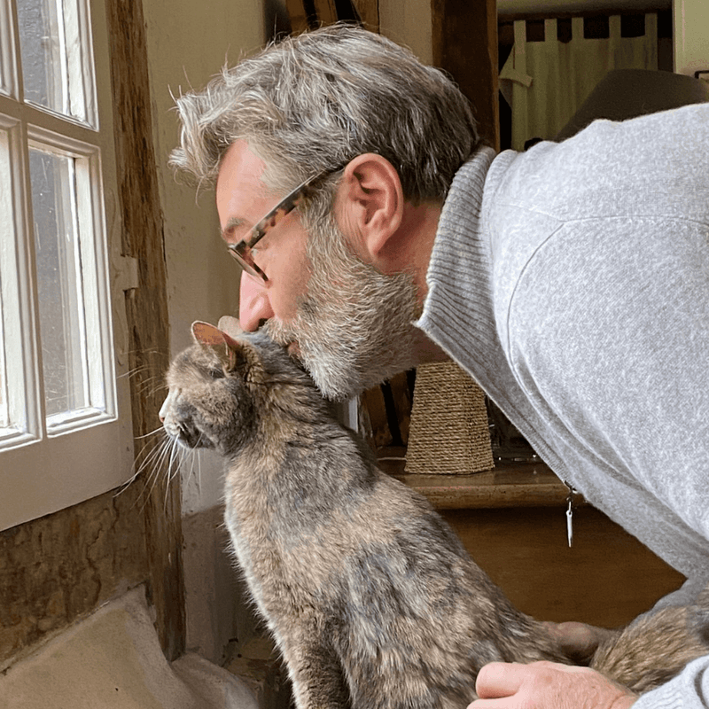 Stan de Vion fondateur de Stan Bio câlinant tendrement son chat tabby gris près d'une fenêtre dans sa maison de campagne