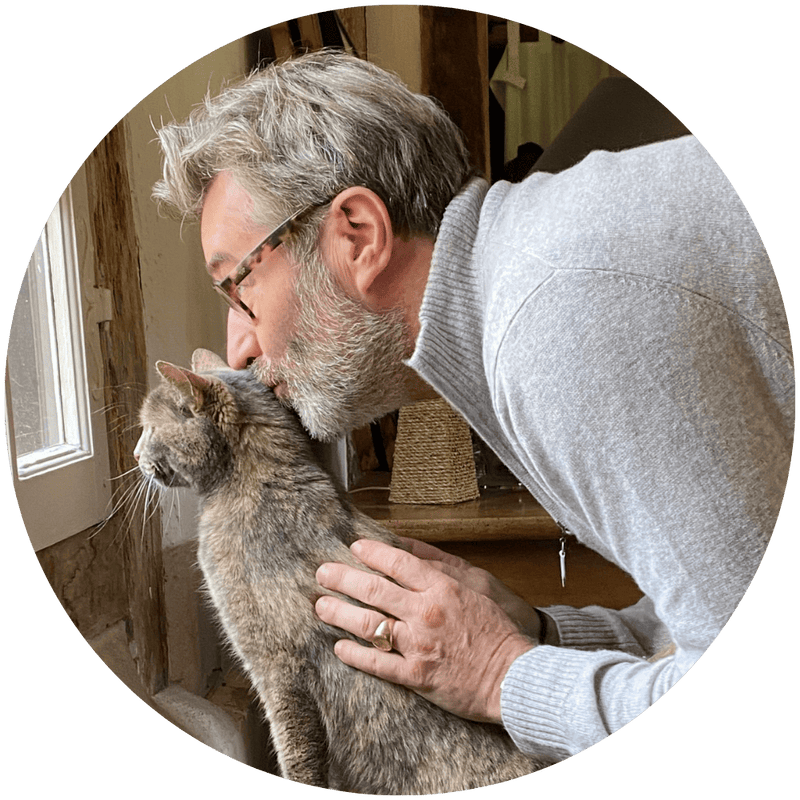 Stanislas, fondateur de Stan.bio, faisant un câlin à son chat gris dans un intérieur chaleureux en pierre apparente